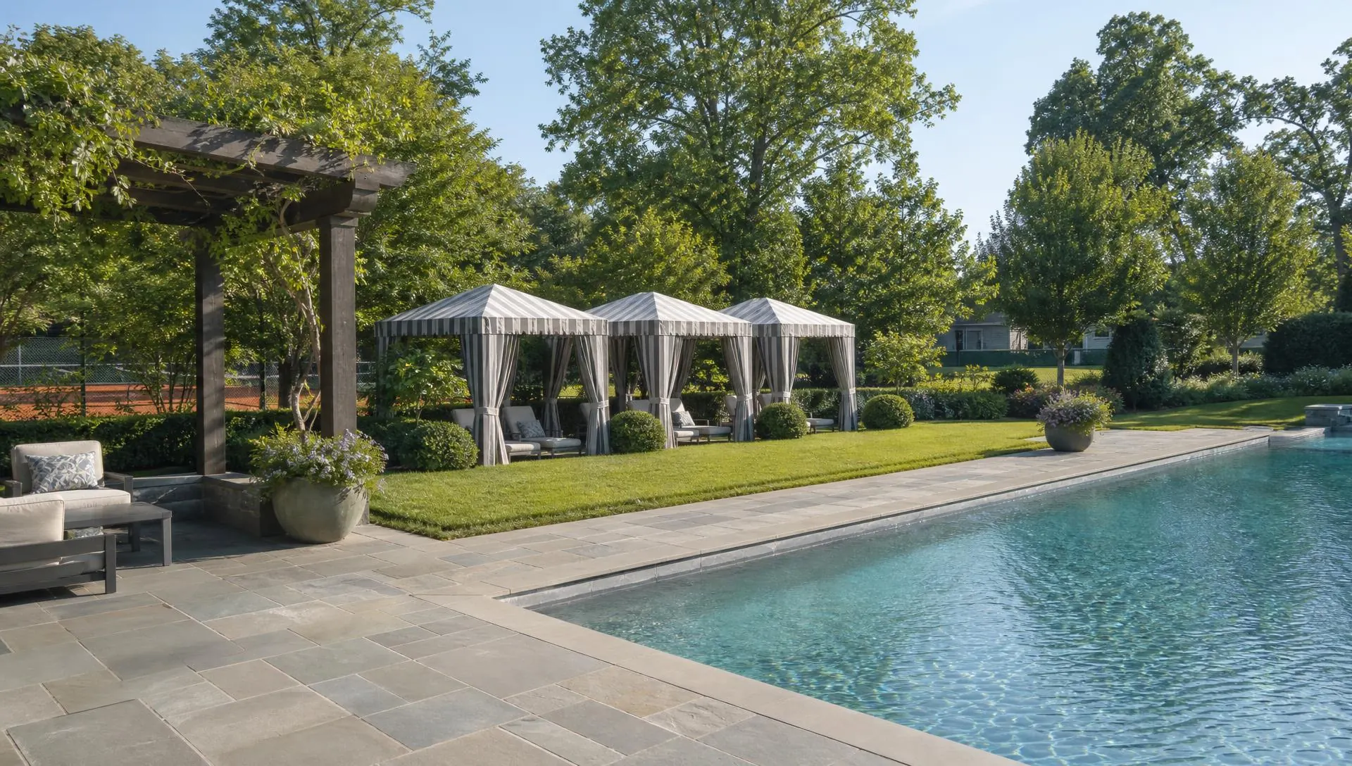 Resort pool terrace with striped cabanas and clay courts beyond at The Palisades
