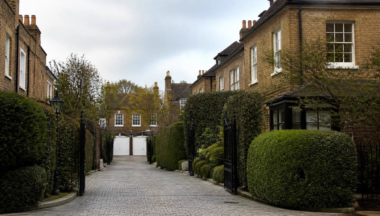 Gated lane of English-influenced brick residences with clipped hedges in Westerham
